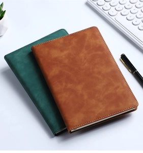 Brown and green leather business notebooks on a white desk with pen and keyboard