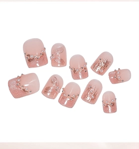 Détail de faux ongles rose œil-de-chat avec perles 3D et motifs en relief dorés