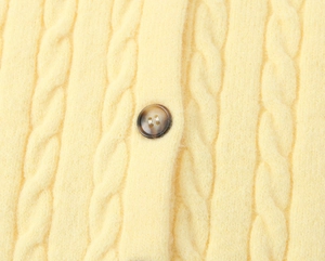 Macro detail of cable-knit texture and amber button on a light yellow cardigan