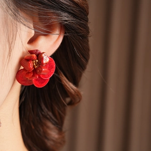 Macro shot of red layered flower earrings with golden beads on a female model's ear
