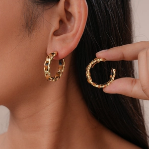 Gros plan détaillé des boucles d'oreilles dorées en C avec texture cuir tressé