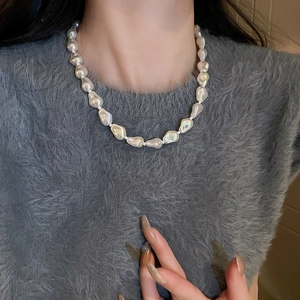 Detail of irregular baroque pearl necklace on a grey sweater showing white pearl luster