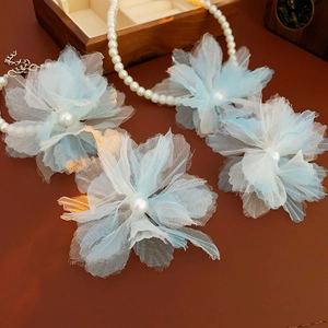 Detail of light blue mesh flower hair clips and white pearl necklace on dark leather surface