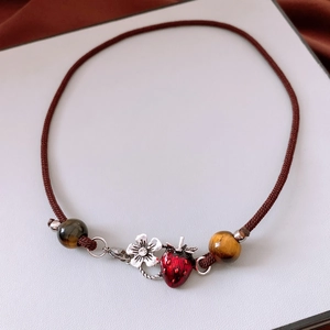 Detailed view of necklace with tiger eye beads, strawberry charm and silver flower pendant
