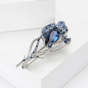 Exquisite silver feather brooch with blue crystals on a white geometric platform