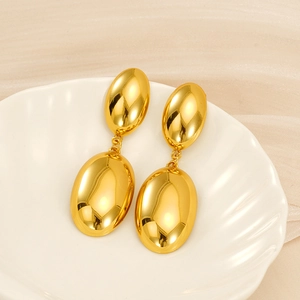 Détail de boucles d'oreilles dorées ovales polies sur un plat en forme de coquille