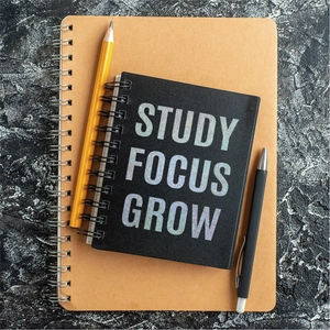 Top view of black and brown spiral notebooks with STUDY FOCUS GROW print and pens