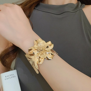 Detailed close-up of a large gold metallic flower cuff bracelet on a female wrist