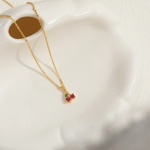 Close-up of cherry pendant with red and green crystals on a gold chain in a ceramic dish