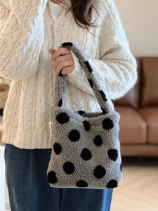 Gros plan d'un sac à main en peluche grise à pois noirs porté avec un gilet blanc doux