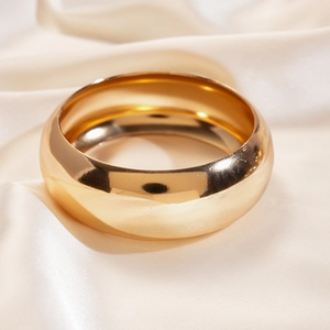 Macro shot of wide chunky gold bangle with a mirror finish on elegant silk fabric