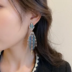 Elegant emerald blue crystal fringe drop earrings with gold-plated metal tassels on a model