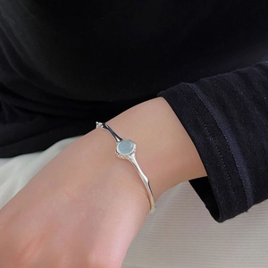 Detail of a minimalist 925 silver irregular open bangle with a light blue crystal gem
