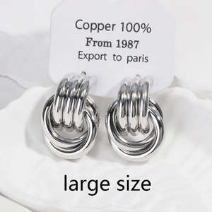 Detail of large silver twisted knot copper earrings on textured white pedestal