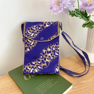 Purple knitted leopard print mini crossbody phone bag on a wooden table with home decor