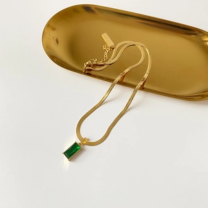 Macro shot of gold flat snake chain with emerald green rectangle zircon pendant