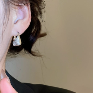 Macro shot of silver-toned textured geometric earring worn on a model's ear