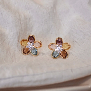 Macro shot of gold flower earrings with multicolored faceted gemstones on linen background
