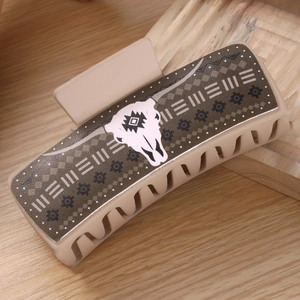 Detail of khaki hair claw clip with ox skull pattern and ethnic motifs on wooden surface
