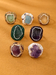 Macro detail of seven irregular raw gemstone rings with crystal pavé on yellow fabric
