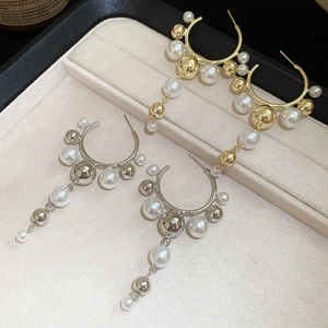 Detail shot of gold and silver pearl tassel C-shaped earrings on jewelry display tray