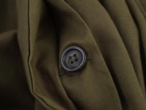 Macro du tissu tissé vert olive avec détail de bouton sombre sur une robe mi-longue