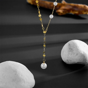 Detail of gold Y-necklace with white pearls on a minimalist textured stone background