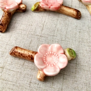 Detail of pink plum blossom ceramic chopstick rest on brown branch with green leaf