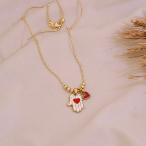 Golden Hamsa hand necklace with red heart pendant on soft beige fabric background