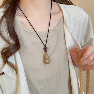 Detail of wooden gourd pendant with red beads on a black cord necklace for women
