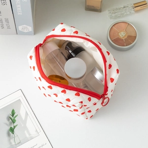 White cotton toiletry bag with red heart patterns and travel bottles inside