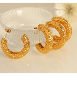 Detailed macro view of gold C-shaped earrings with hammered lava texture and matte finish