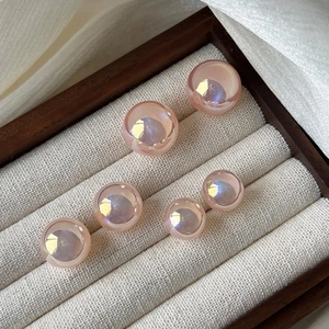Pink iridescent round pearl stud earrings in three sizes on a wooden display case
