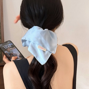 Detail of a light blue satin oversized scrunchie shown on a ponytail with silk texture