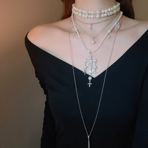 Macro detail of multilayer pearl necklace featuring a diamond-set cross pendant on a model