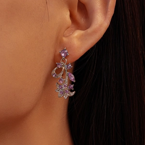 Detailed side view of leaf and flower drop earrings with purple zircon on a model