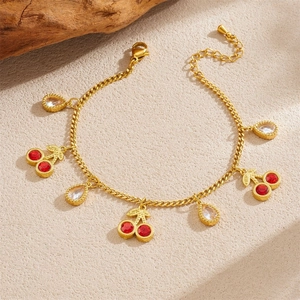 Elegant gold cherry bracelet with red gemstones and teardrop crystals on beige background