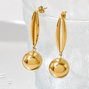 Polished gold stainless steel hollow ball drop earrings on glass with water droplets