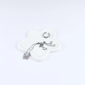 Detailed macro of pink butterfly necklace and silver ear cuff in flower ceramic tray