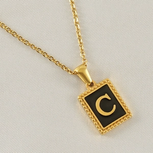 Macro detail of gold necklace with black enamel rectangle pendant featuring letter C