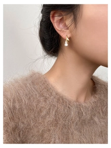 Close-up of minimalist gold drop earrings with white irregular pearls on a female model