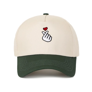 Close-up of heart finger gesture embroidery on a cream and forest green contrast baseball cap