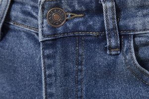 Detailed close-up of metal button and reinforced stitching on blue washed denim jeans