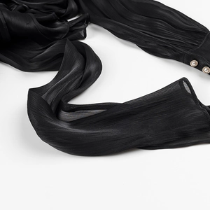 Detail view of black pleated fabric featuring elegant pearl buttons on the sleeve cuff