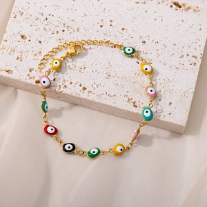 Golden chain bracelet with colorful Evil Eye charms and lobster clasp on stone tray