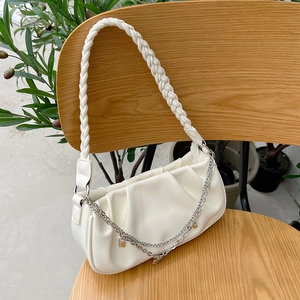 Detailed shot of white pleated cloud bag with woven strap and silver chain on a chair