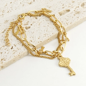Double-layered 18k gold stainless steel key pendant bracelet on a stone pedestal