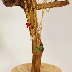 Close-up of butterfly necklaces in four colors hanging on a rustic wooden stand