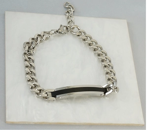 Détail d'un bracelet gourmette en acier inoxydable argenté avec insert noir sur marbre blanc