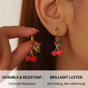 Macro shot of gold-plated cherry earrings with red enamel glaze and green leaf detail